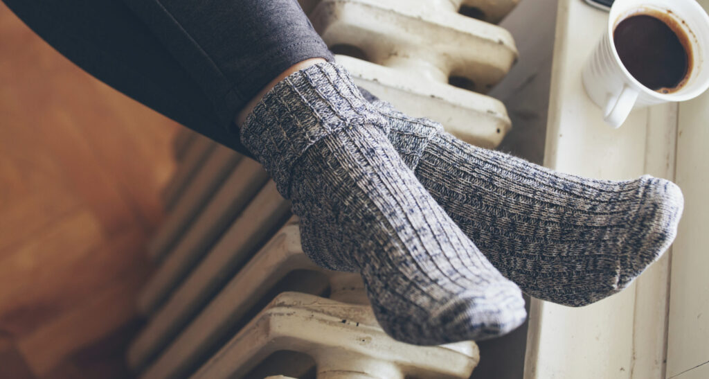 Ett par fötter vilar mot ett element. En kopp kaffe syns i bakgrunden.