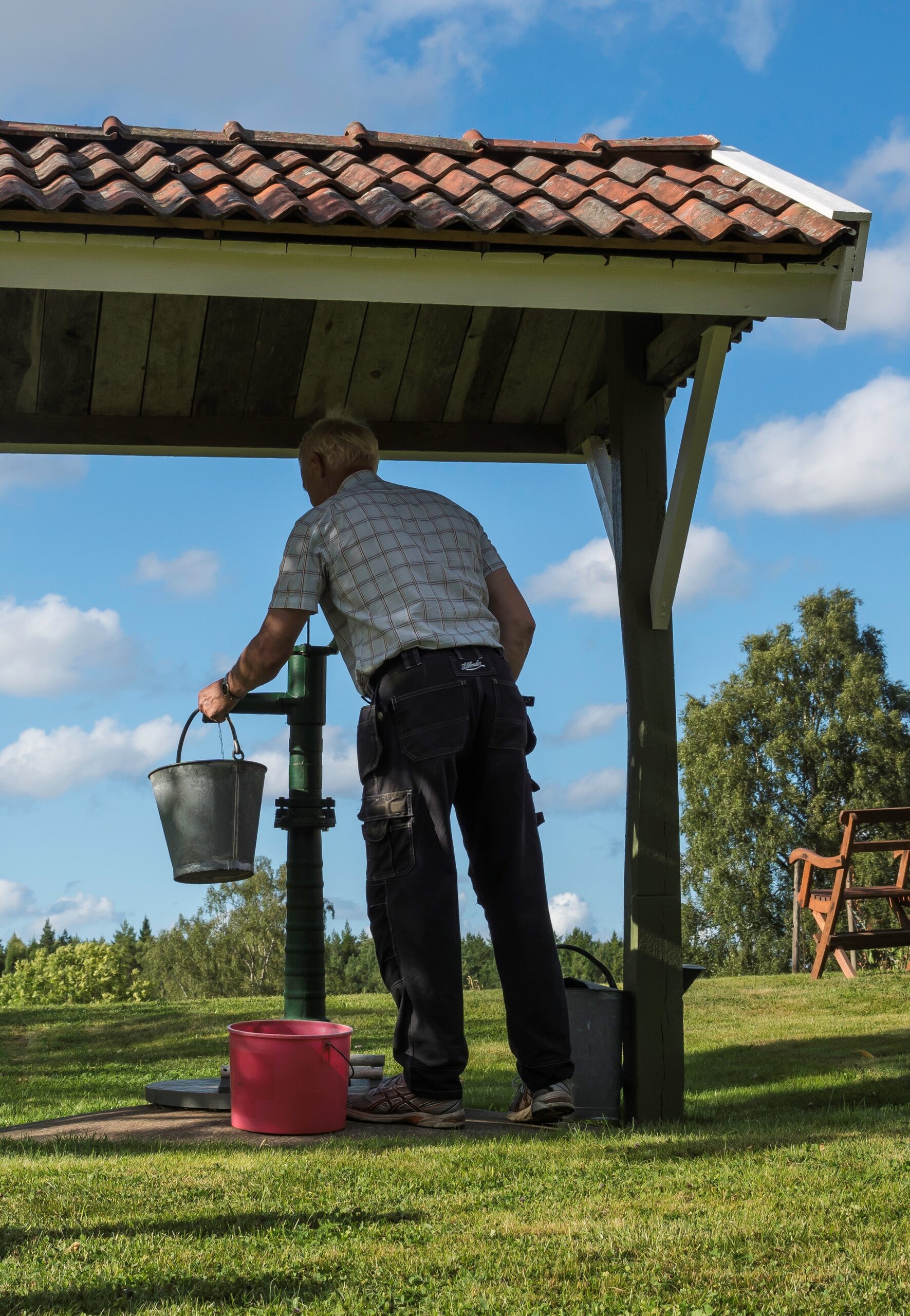 10573994-vattenpump (2) En man pumpar vatten vid en grön vattenpump.